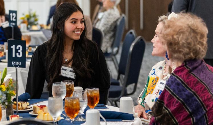 Female student sitting at a table with two women eating a meal 