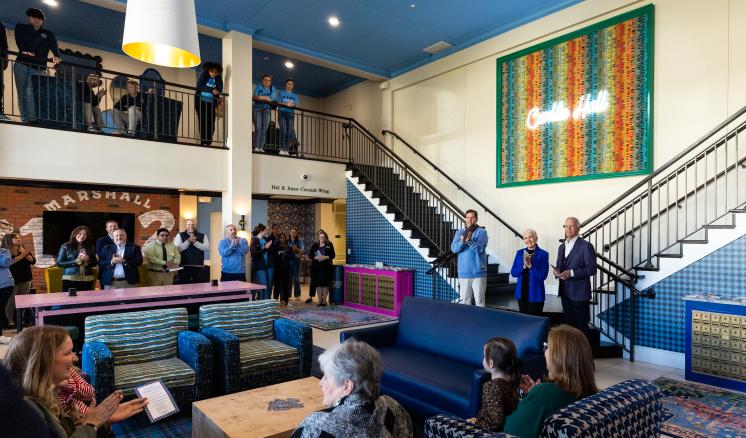 Men speaking in front of crowd in residential hall lobby 