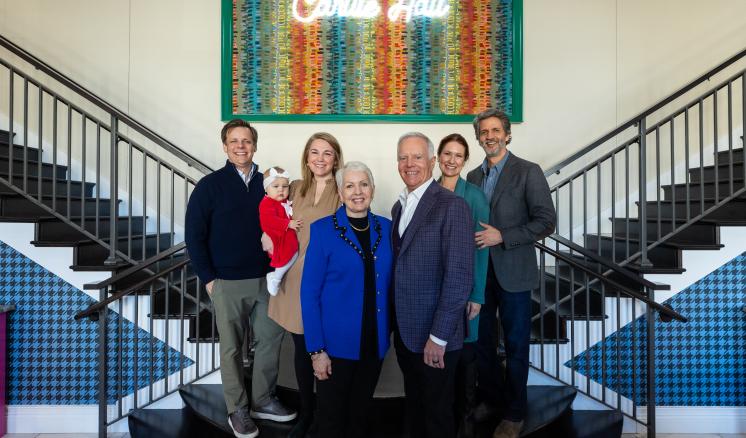 Small group of men and women posed on stair case in residential hall lobby smiling at camera 