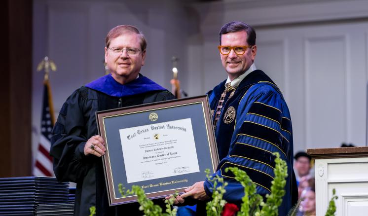 Two men in academic regalia holding diploma 