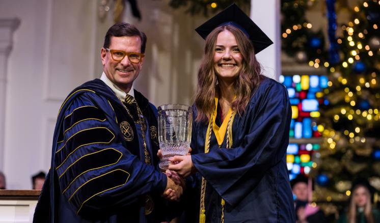 Man in academic regalia awarding student in navy cap and gown with Presidents award 