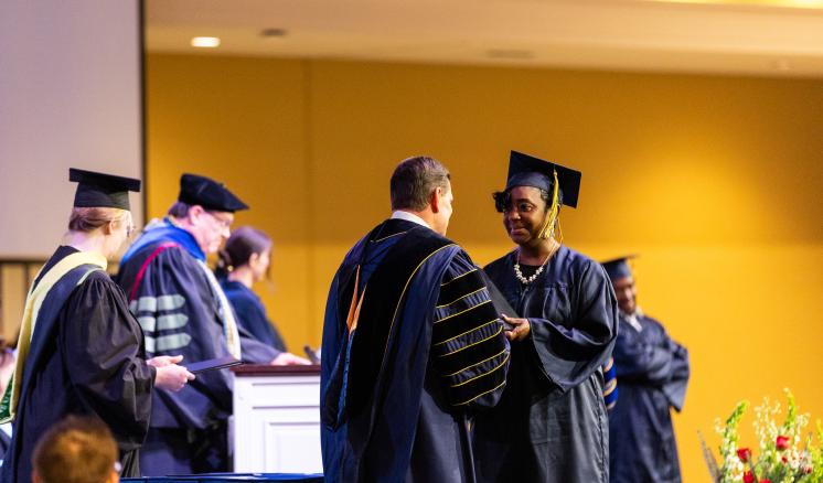 Student in navy cap and gown being awarded diploma on stage at graduation 