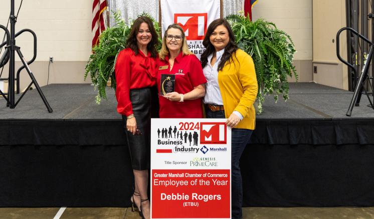 Three women posing with employee of the year award smiling at the camera 