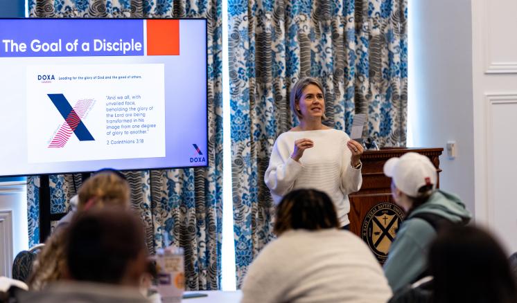 Woman speaking with a presentation of the screen to a group of people 