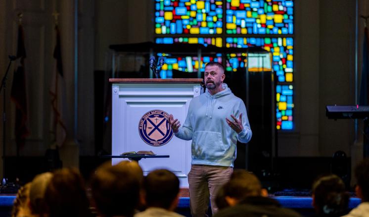 Man speaking on a stage in front of an audiene in a chapel 