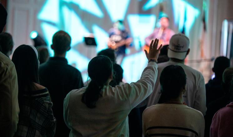 Women worshiping with her hand in the air in a dark room 