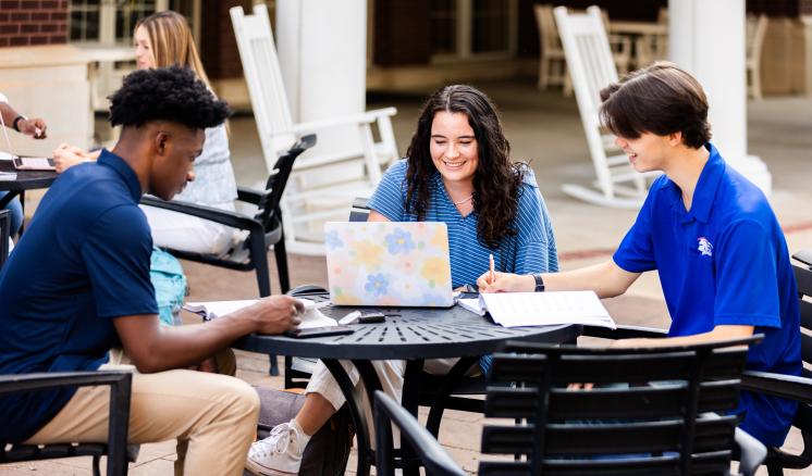 Three students sitting at a table outdoors doing school work 