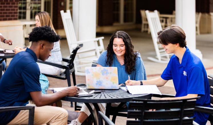 Three students sitting at a table outdoors doing school work 