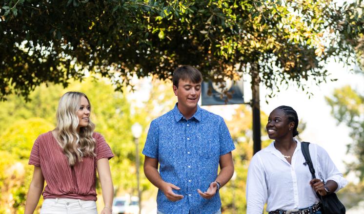 2023_student_photoshoot_september_2023_0087 Three students talking and walking together on a sidewalk outdoors