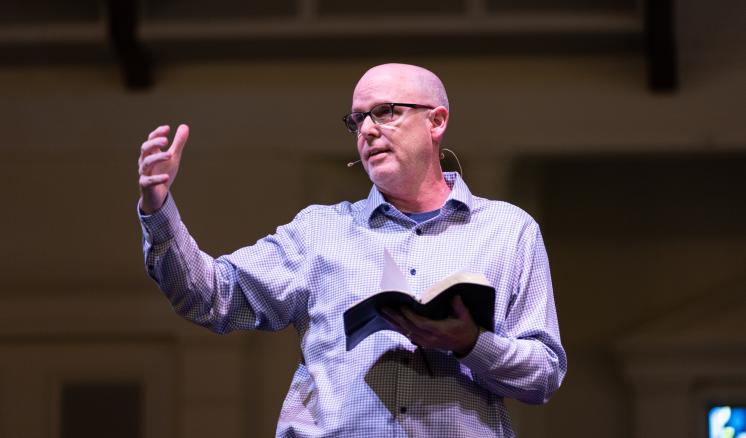 Man speaking on a stage with a Bible in his hand 