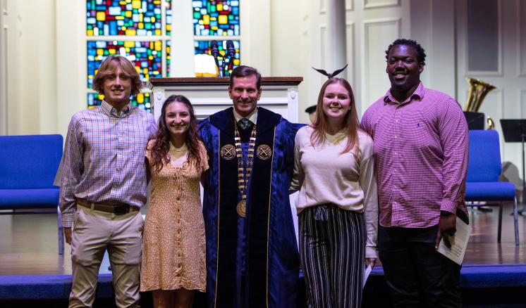 20240909_convocation_0421 Four ETBU students pose for a photo with University President J. Blair Blackburn, who is dressed in academic regalia