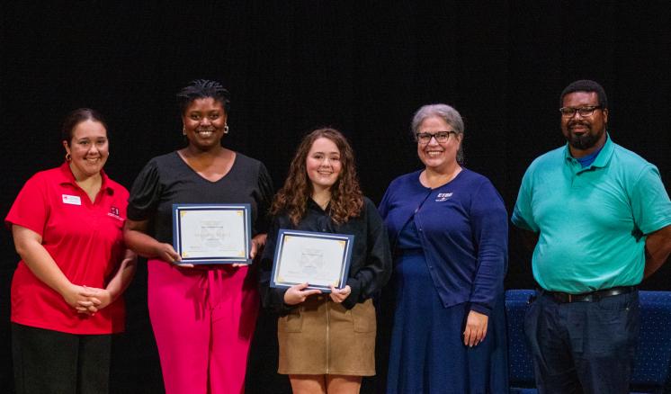 Two Students pose with awards alongside three judges on a stage