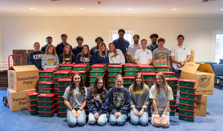 2024_operation_christmas_child_0231 More than a dozen students stand around large stacks of Christmas boxes filled with donations