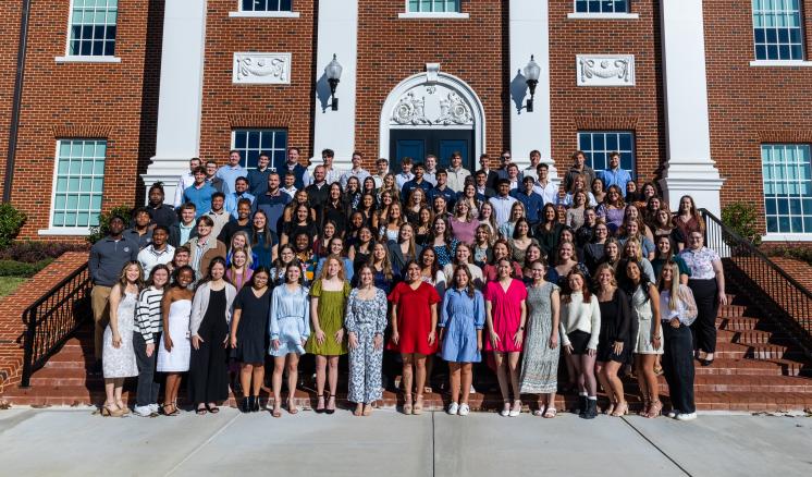 Large group of students stand on a staircase behind an academic building on a university campus