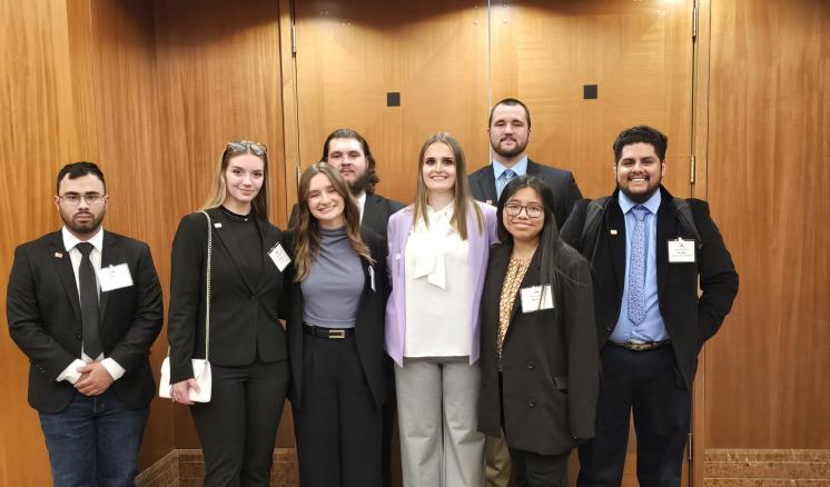 Eight students stand side by side in business professional attire with name badges on.