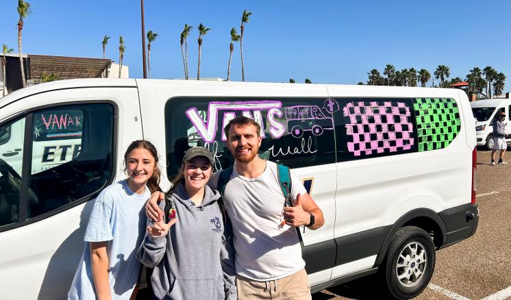 A group of 3 people stood infront of a Van outside in a parking lot