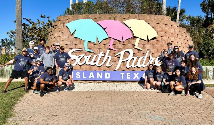 A group of people standing in front of a brick wall with South Padre Island Texas written on it