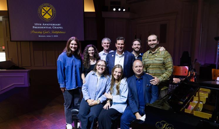 A group of people in a dark lit stage posing together, some standing, some sitting down