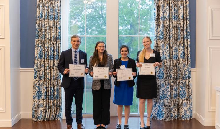 4 people stood in front of a bright window holding up awards in business professional clothing
