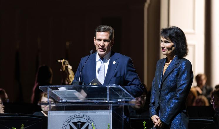 A man and a woman stood behind an acrylic podium in a dimly lit area