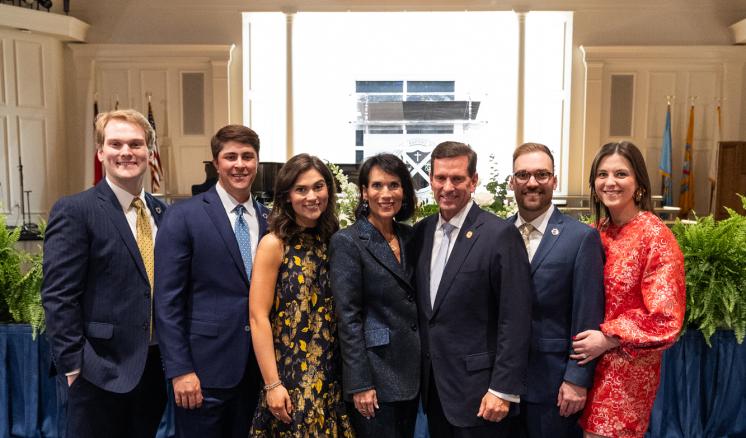 7 people stood around in a well lit room posing together for a group photo