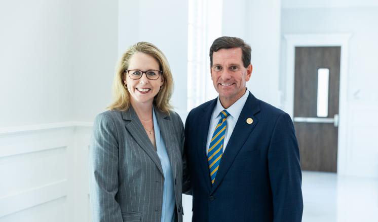 Two people stood in a brightly lit room wearing formal clothing smiling