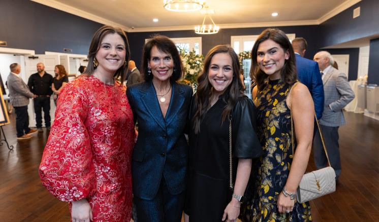 4 women stood in a brightly lit room with a crowd of people behind them
