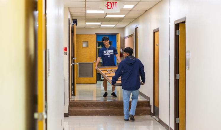 2 guys carrying a large table upstairs in a well-lit room