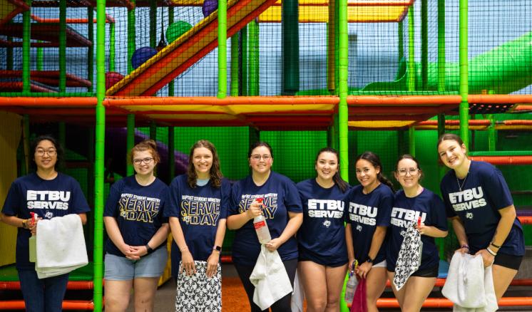 A group of people wearing ETBU Serves shirts standing in front of a play place