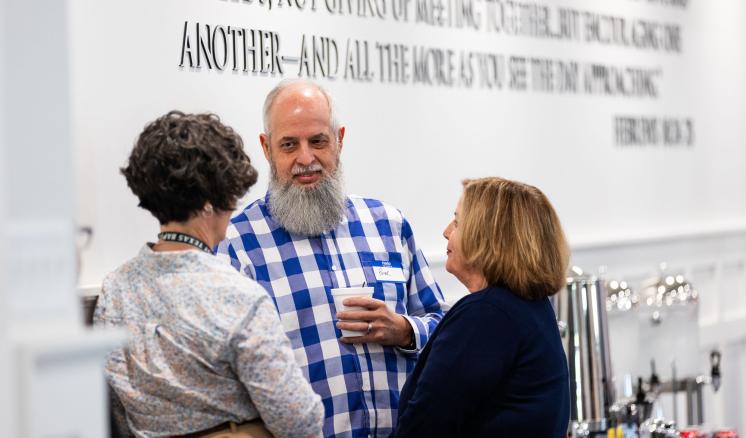 A man and 2 women looking at eachother standing in a circle in front of a board with a bible verse