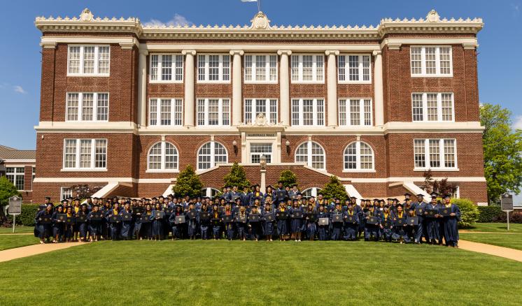 Spring 2025 Commencement A large group of graduates in graduation regalia stand in front of ETBU's Historic Marshall Hall