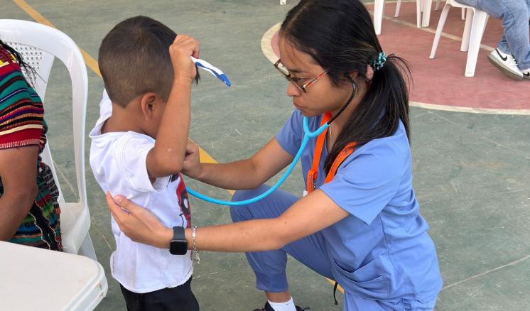 A woman in nursing scrubs holding a child by the waist giving a physical exam
