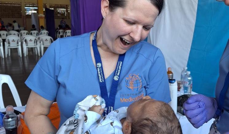 A woman in nursing scrubs holding an infant child with a lanyard around her neck