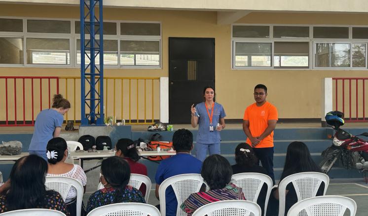 2 speakers stood upfront in front of a small crowd one wearing nursing scrubs the other in an orange t-shirt