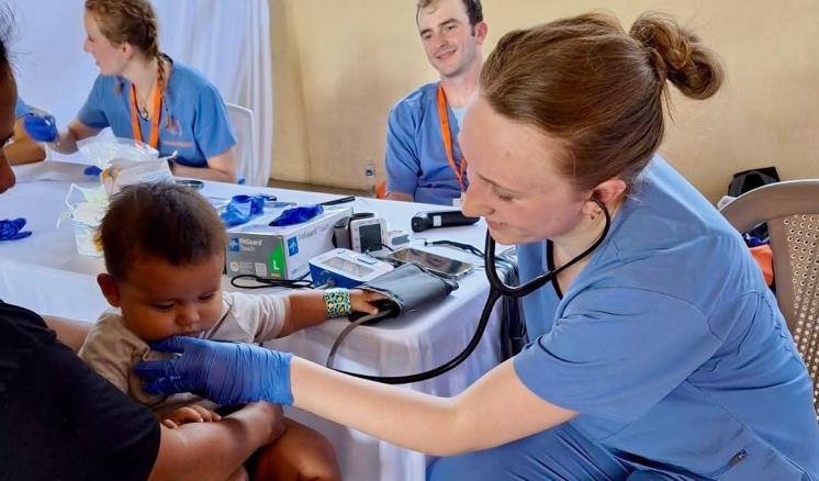 A woman tending to a pediatric patient wearing scrubs inside with a stethoscope