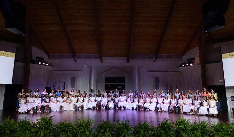 A large group of people in white clothing sitting on a dimly lit stage