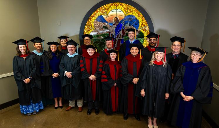 People standing inside in academic regalia infront of a stained glass window