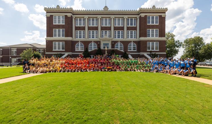 A group photo of a large group of student standing in front of a brick building