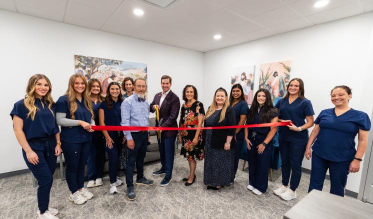 A group of people stood in a room with large scissors cutting a bright red ribbon
