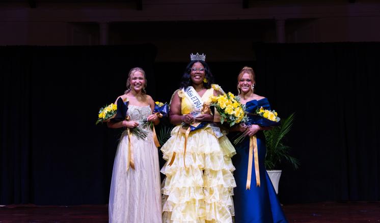 A group of women standing on a stage in formal attire