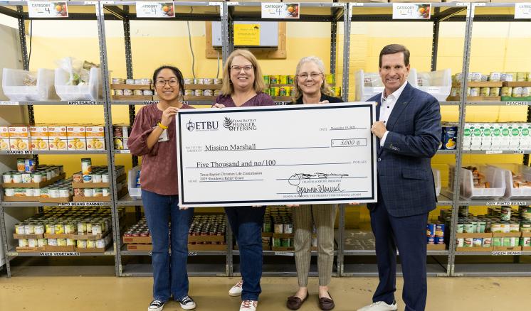4 people holding a giant check inside a warehouse