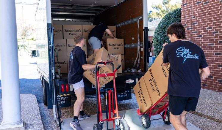 A group of men loading boxes onto a truck with dolly's