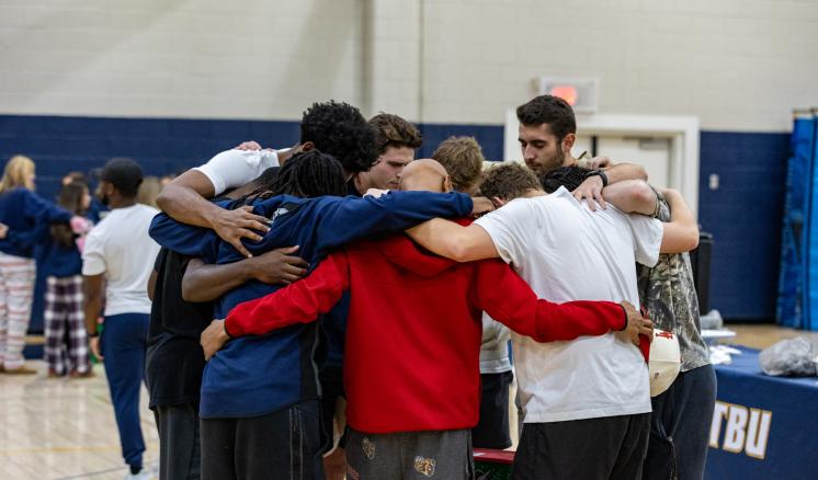 A group of men standing in a huddled circle praying