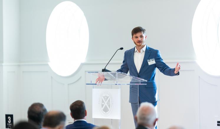 A man in a blue suit stood speaking to an audience at a podium