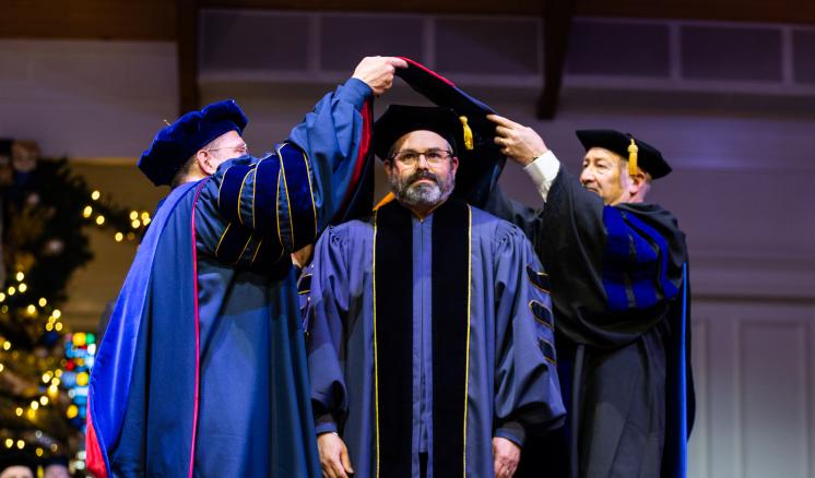 2 men hooding another all wearing academic regalia