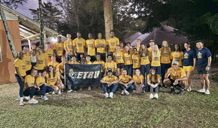 a group of people outside in yellow shirts holding an ETBU flag