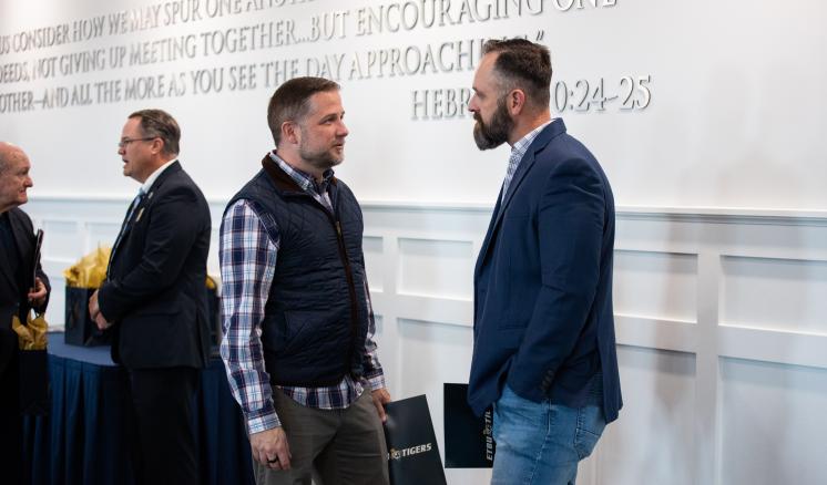 Men standing and talking together in front of a wall with scipture written upon it