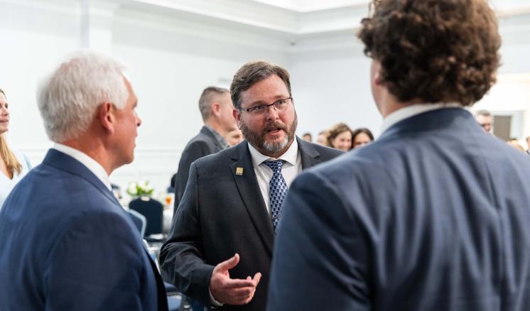 Men standing talking together in a crowded room wearing professional attire
