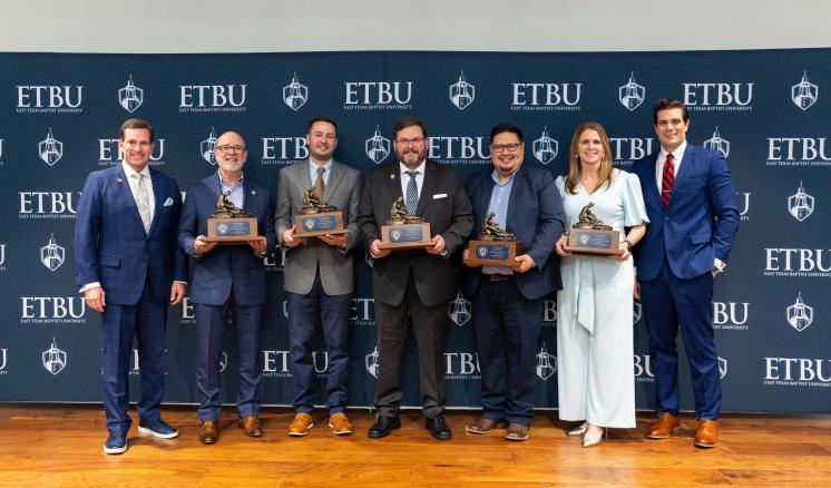 A group of people smiling in front of a backdrop holding awards