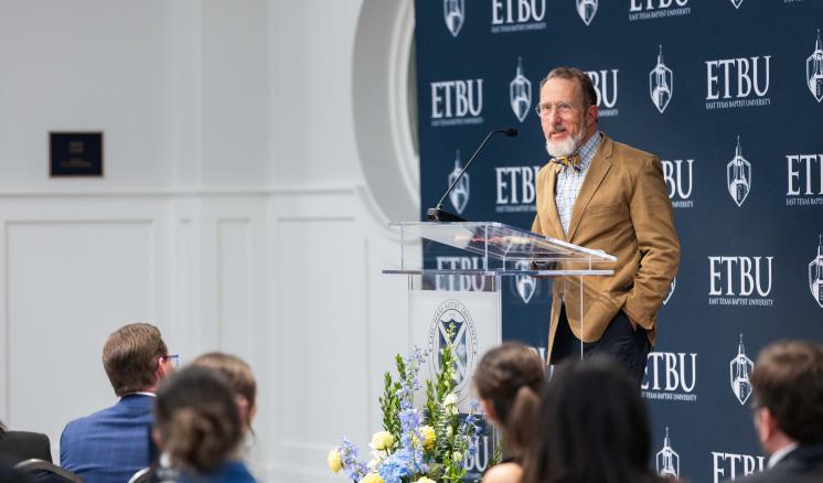 A man speaking behind a podium addressing a crowd inside